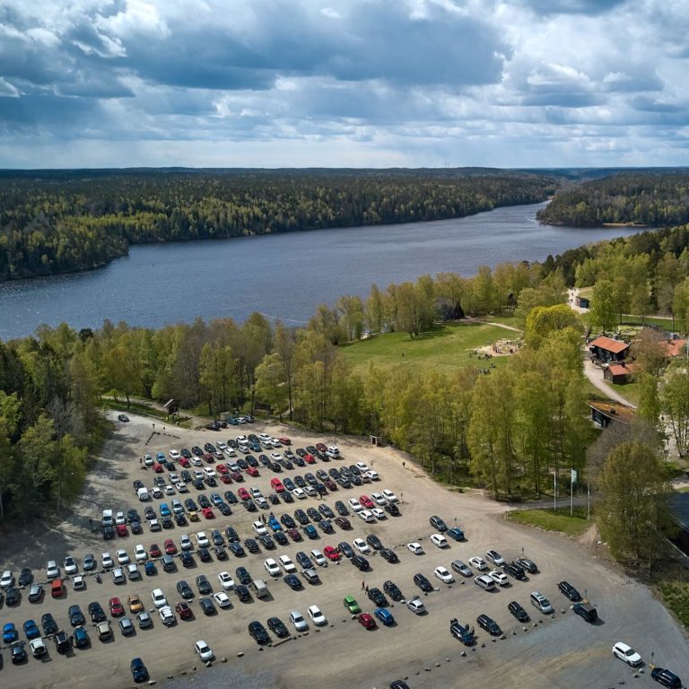 stor parkering med många bilar vid en sjö och en skog