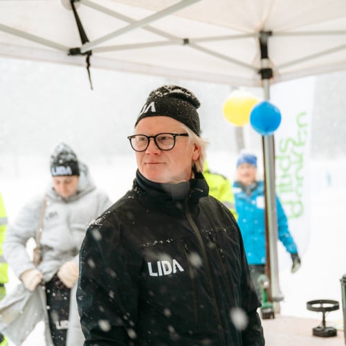 En man i Lida-klädsel som står under ett vitt tält i snön.