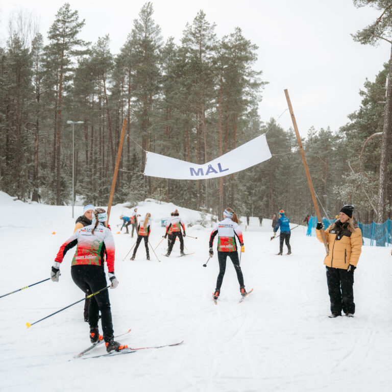 En grupp människor som åker längdskidor förbi en mållinje.