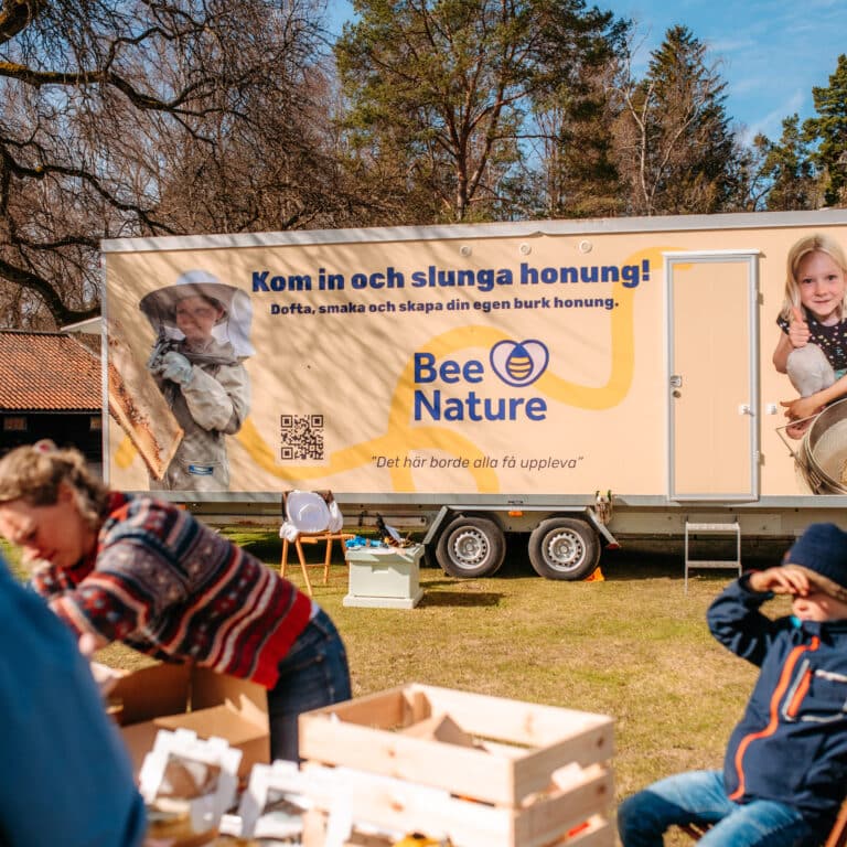 En grupp människor som sitter runt ett bord framför BeeNatures mobila honungsslunga.