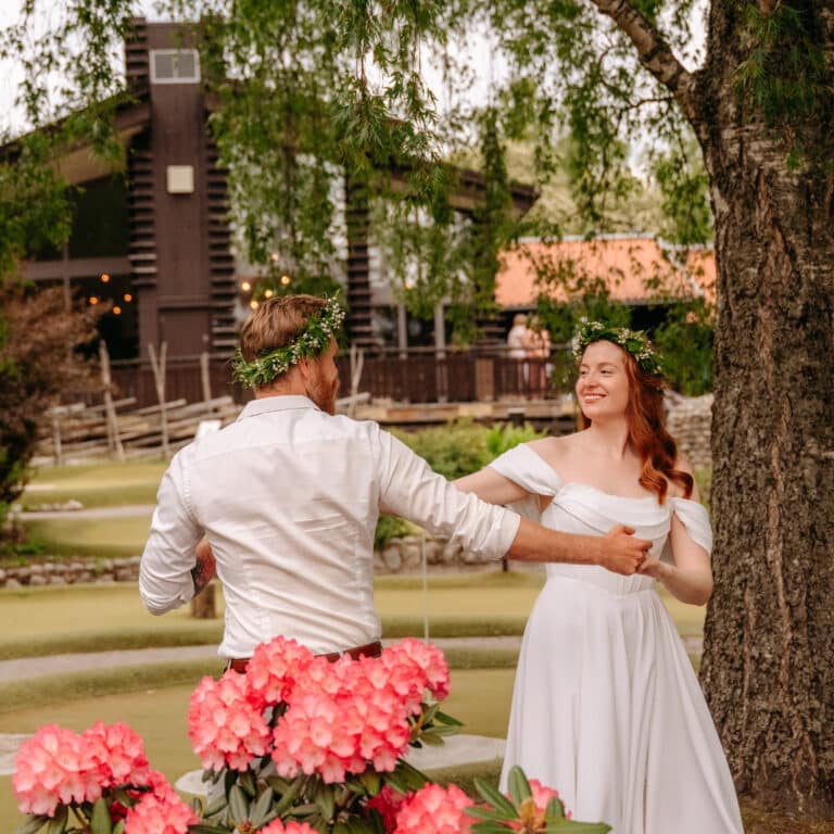 Ett brudpar dansar bakom en blommande rhododendron med Lida Värdshus i bakgrunden.