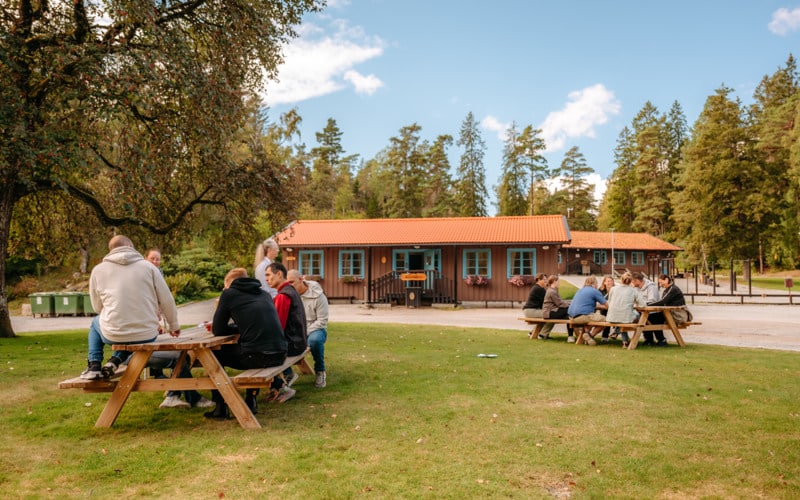 En grupp människor som sitter vid picknickbord utanför konferenslokalen.