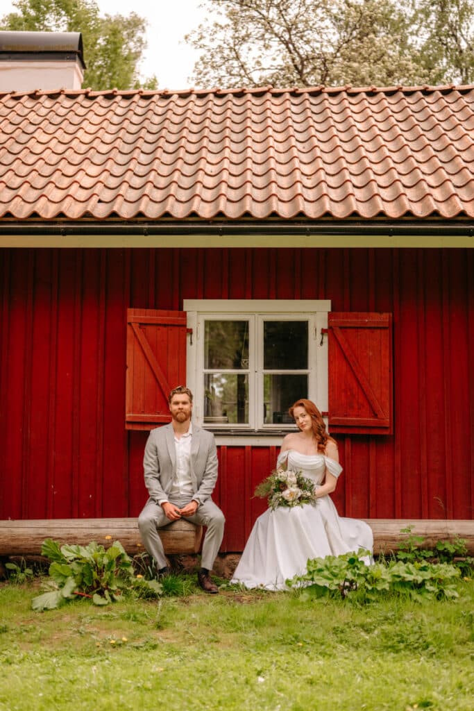 Ett brudpar som sitter på en bänk framför en röd byggnad.